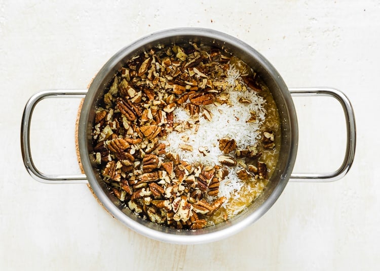Evaporated milk, butter, and brown sugar mixed together in a pot with coconut and pecan on top. 