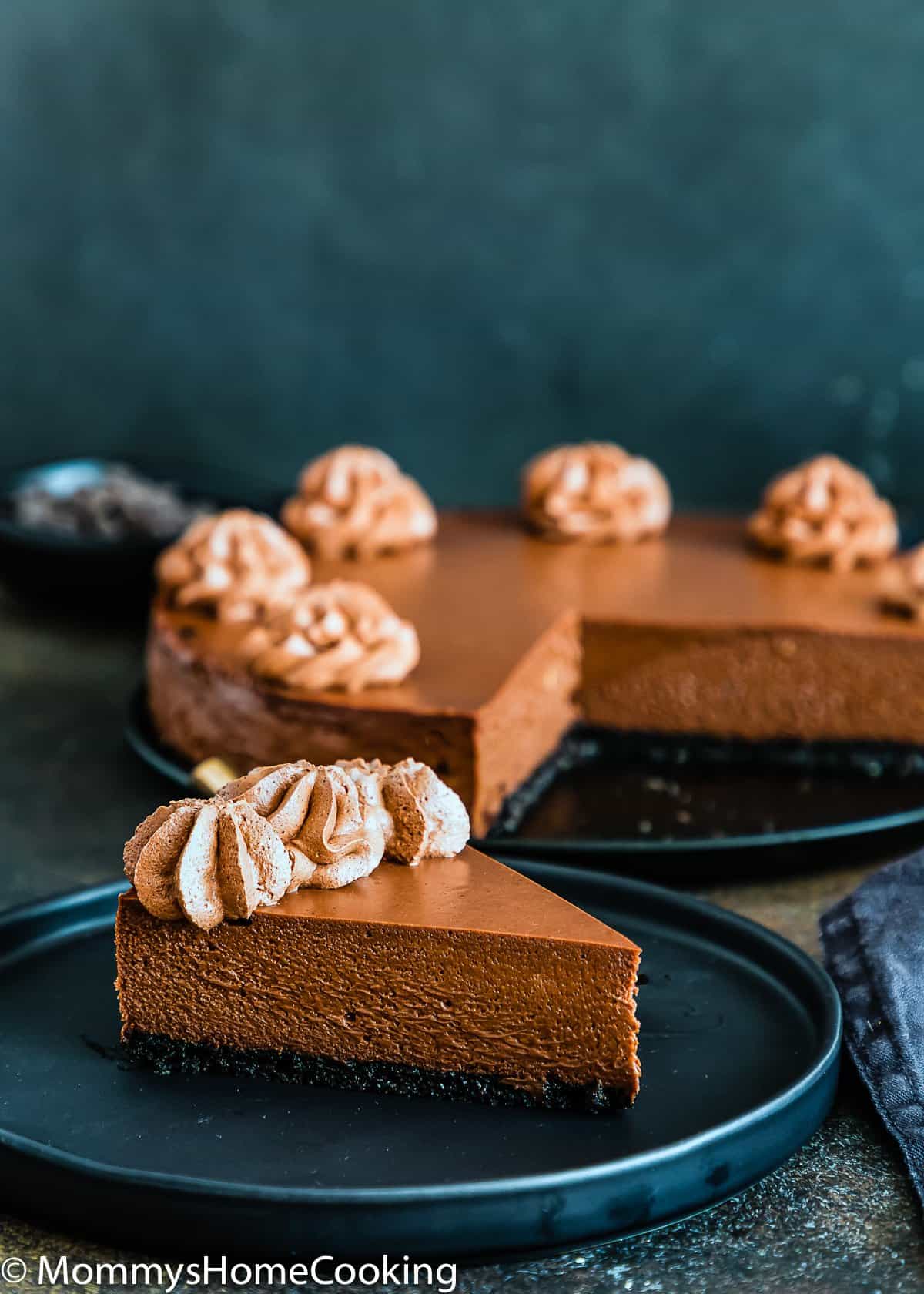 Eggless Chocolate Cheesecake on a plate with the whole cheesecake in the background.