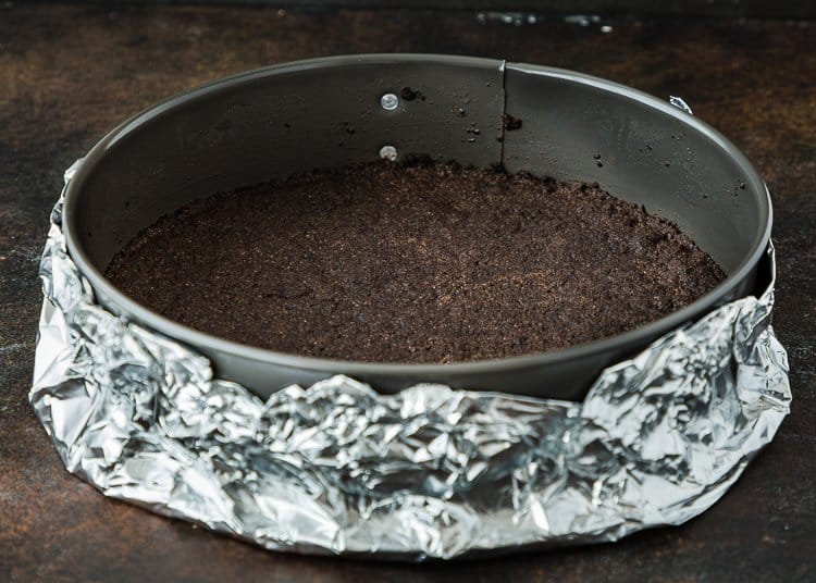 a springform pan with oreo crust over wrapped with two pieces of foil. 