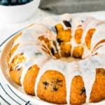 Eggless Lemon Blueberry bundt Cake on a plate with a bowl of blueberries in the backgraound
