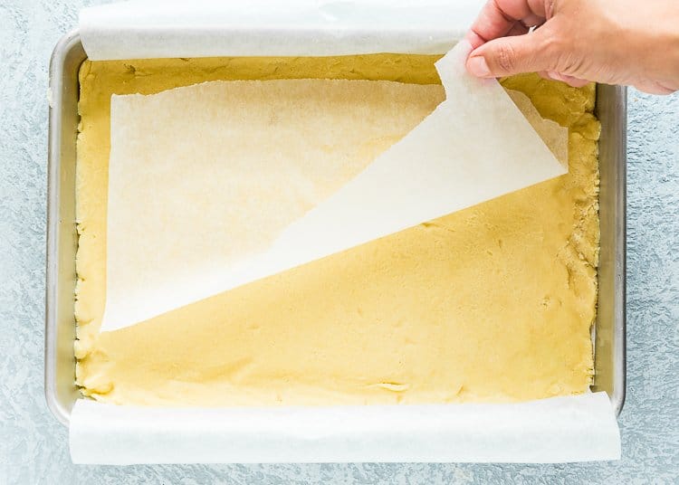 a hand removing parchment paper from the top of the dough to make lemon bar crust.