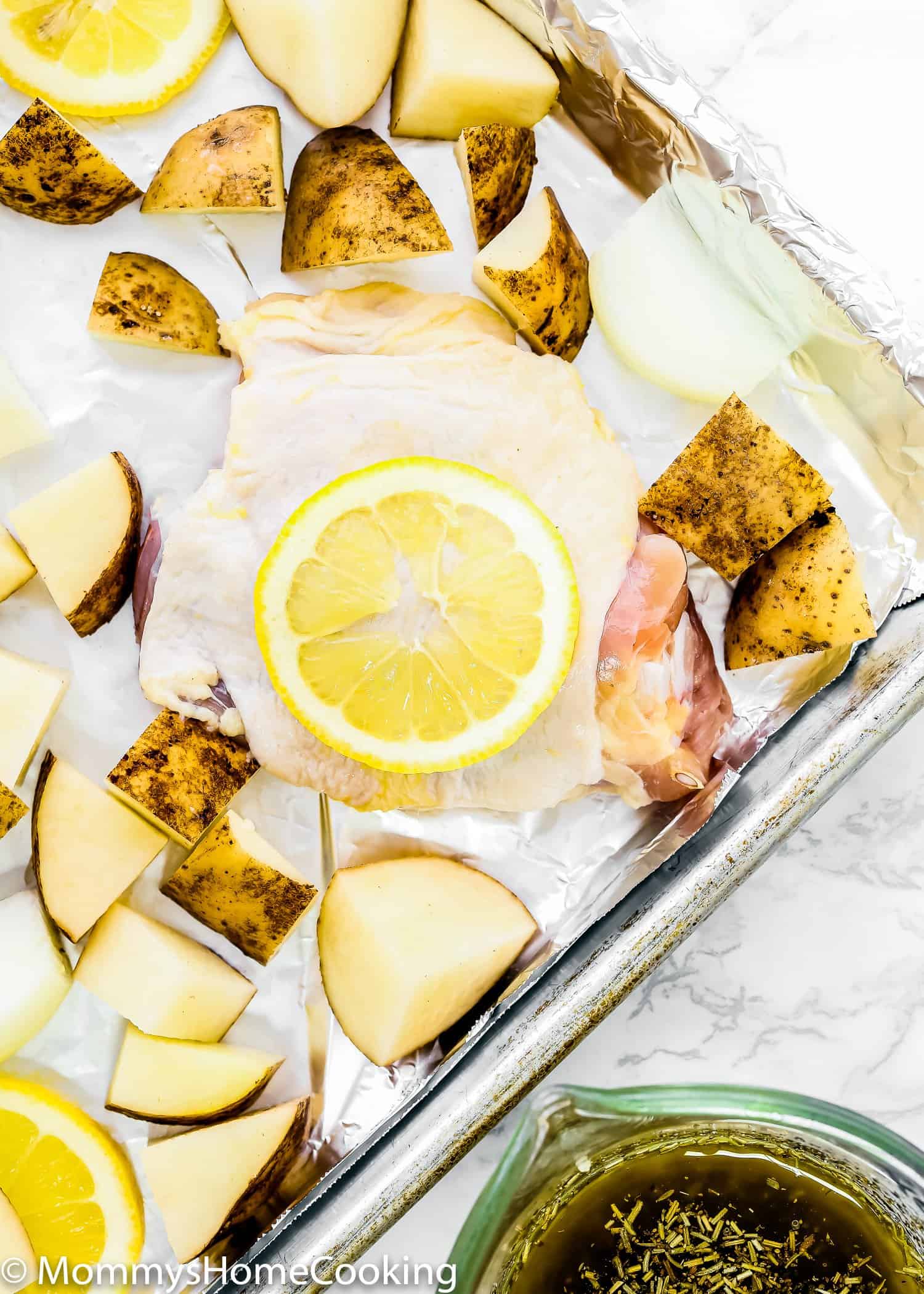 raw chicken, potatoes and lemon slices in a baking sheet.
