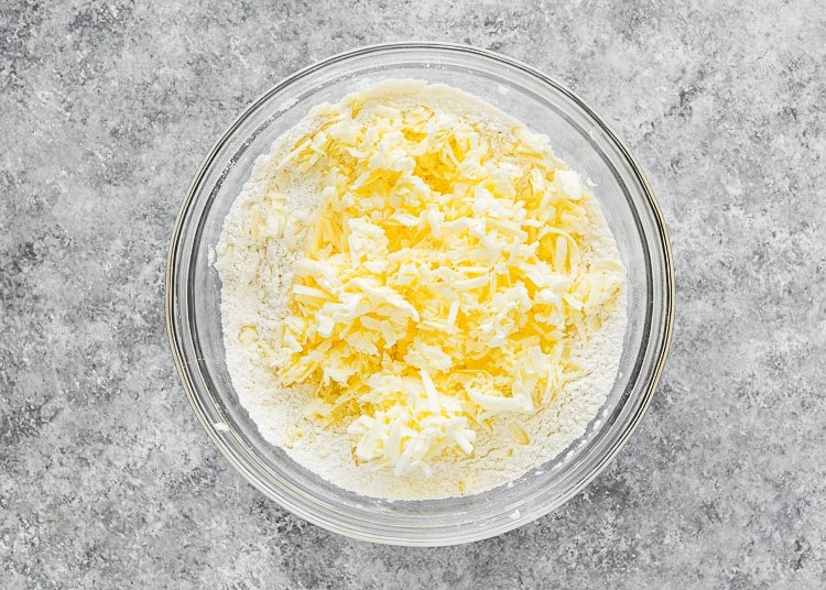 dry ingredients to make eggless biscuits in a bowl with cold grated butter on top.
