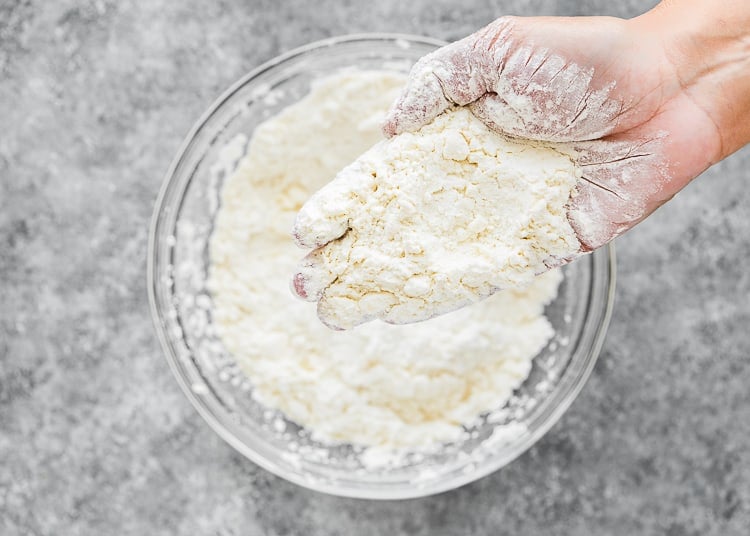 a hand showing mixture to make egg-free biscuits resembling  coarse crumbs. 