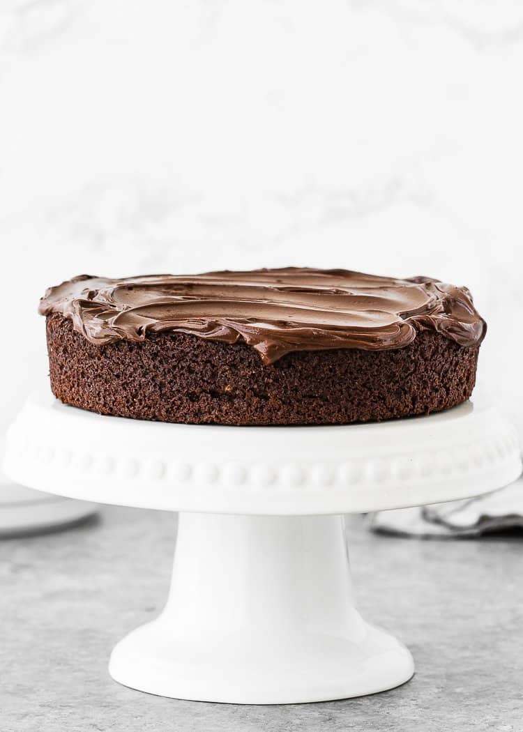 an egg-free chocolate cake over a cake stand covered with chocolate ganache.