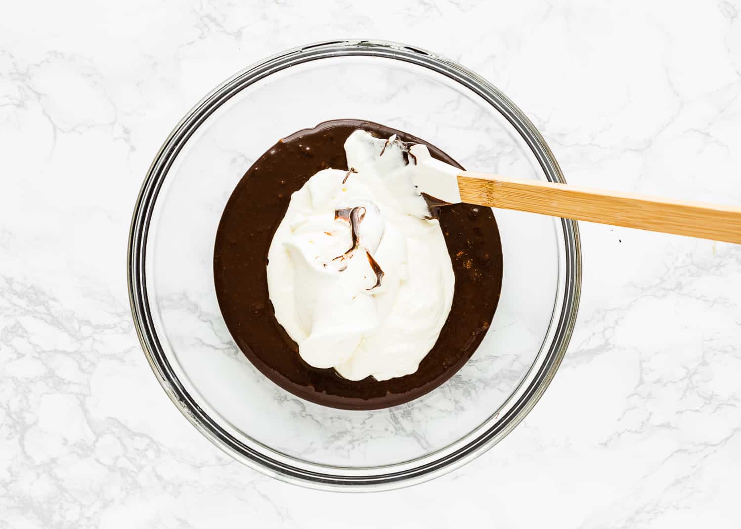 chocolate mixture with whipped cream on top in a bowl with a spatula. 