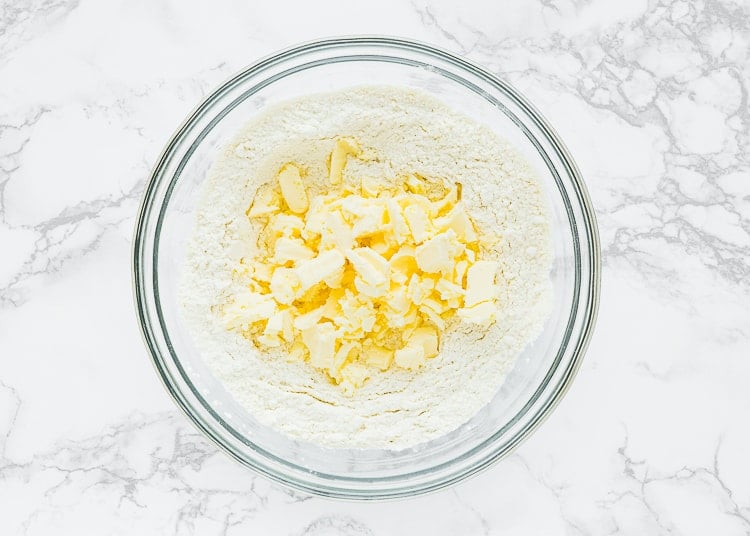 dry ingredients to make eggless scones in a bowl with frozen butter on top. 