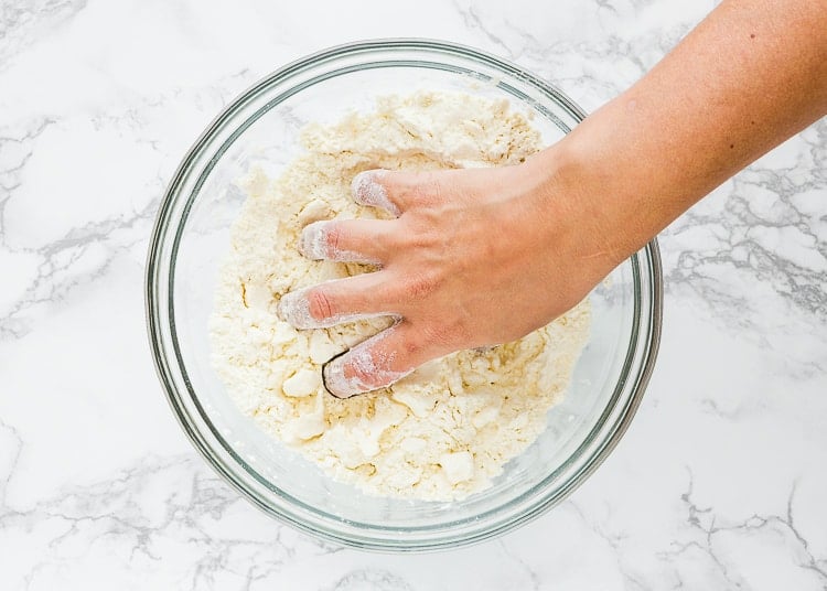 a hand cutting in butter into dry ingredients to make scones. 