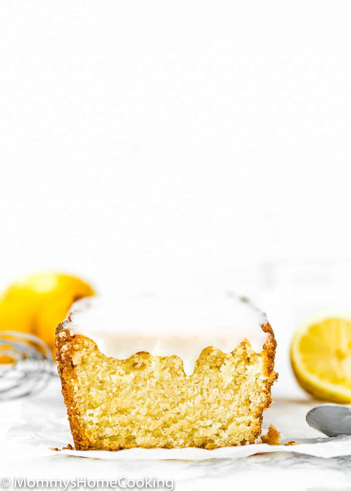 sliced Eggless Lemon Pound Cake with glaze and fresh lemons on the background.