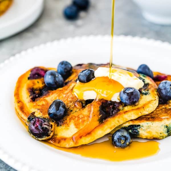 Eggless Blueberry Pancakes with fresh blueberries and butter in a plate drizzled with maple syrup