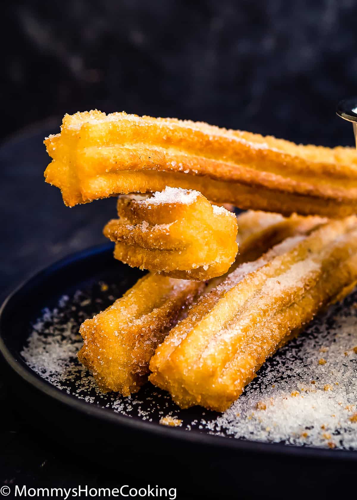 fried churros with sugar on a black plate.