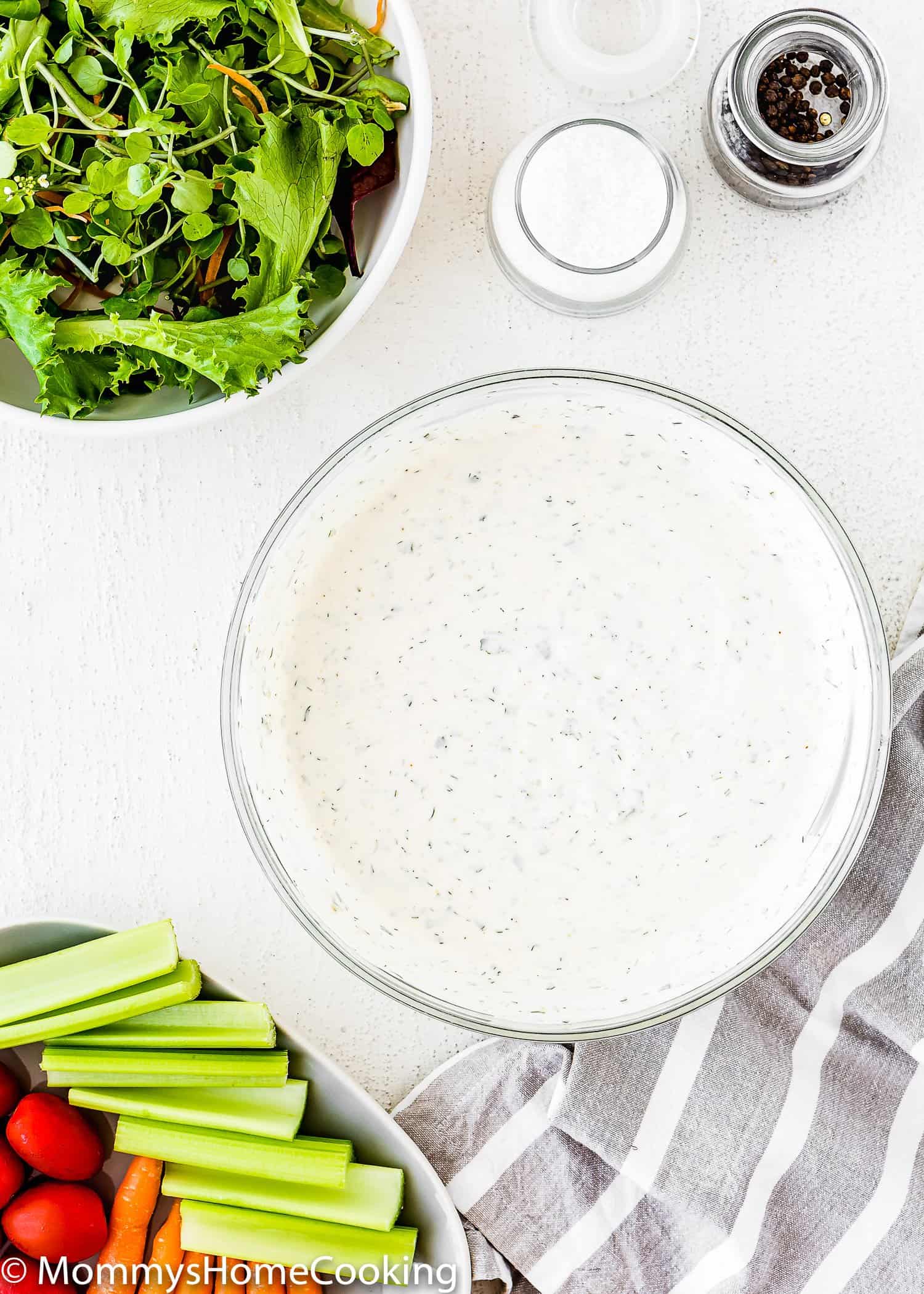 Homemade Eggless Ranch Dressing/Sauce in a mixing bowl with a plate with celery and cherry tomatoes on the side. 
