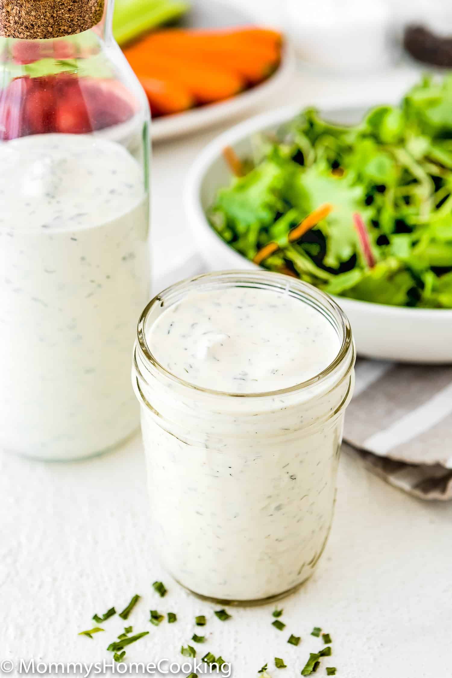 Homemade Eggless Ranch Dressing/Sauce in a jar with a bowl with greens in the background. 