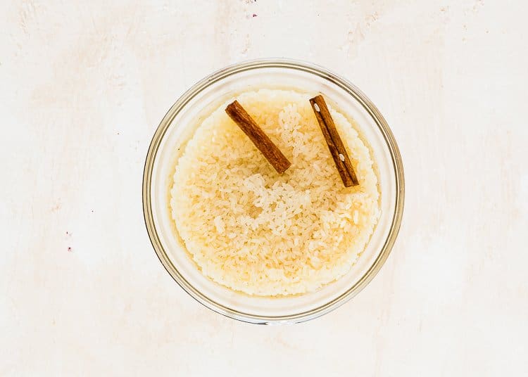 rice, water and two cinnamon sticks in a bowl. 