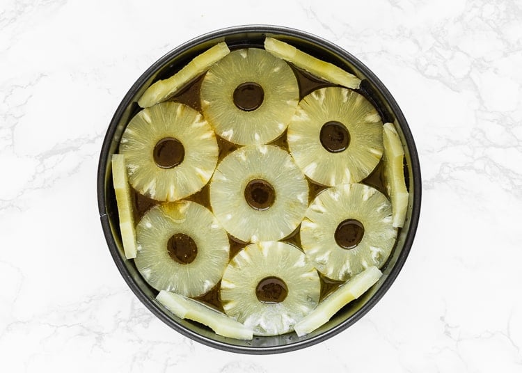 melted butter and brown sugar mix together in a cake pan and topped with pineapple rings.