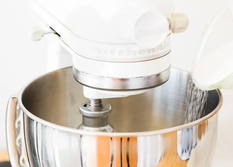 sugar being added to a egg-free meringue into a stand mixer bowl. 