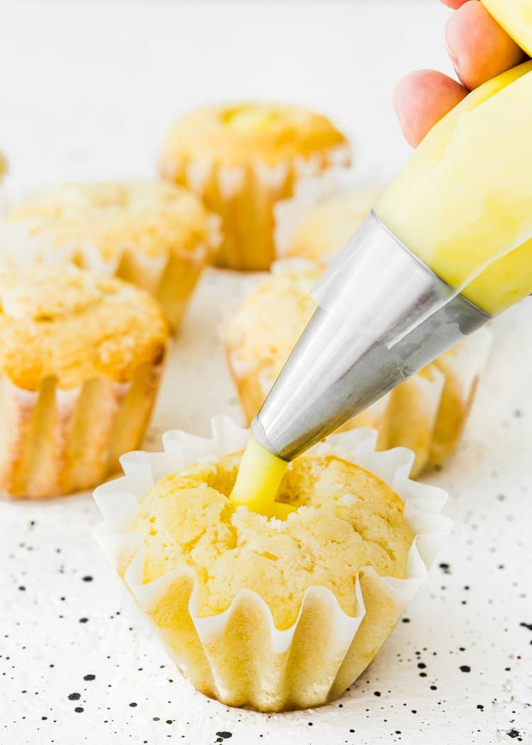 a piping bag filling a egg-free cupcake with eggless lemon curl.