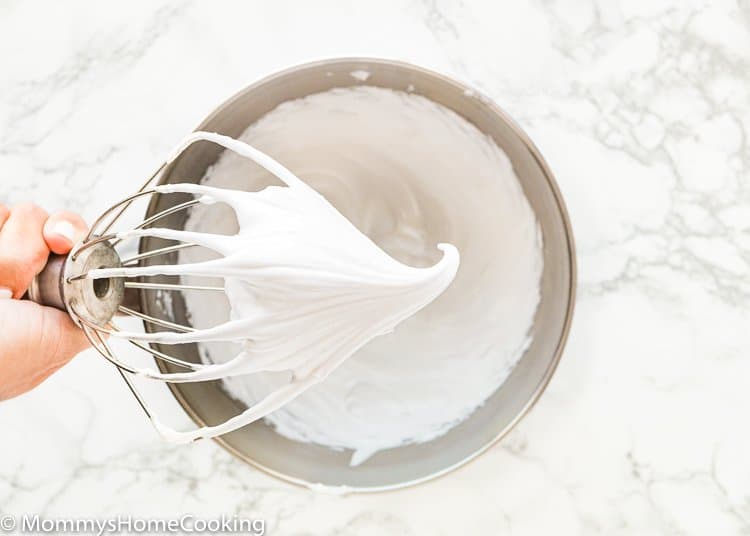 A hand holding a whisk with eggless Meringue.