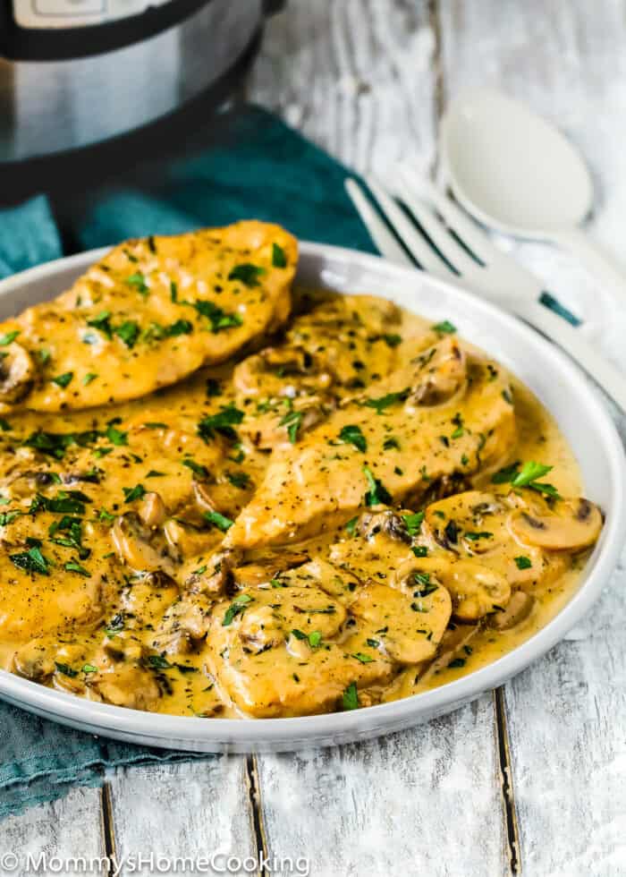 Plate of Easy Chicken Marsala (Instant Pot & Stovetop) with creamy mushroom sauce, garnished with chopped parsley, served on a rustic wooden table with utensils in the background.