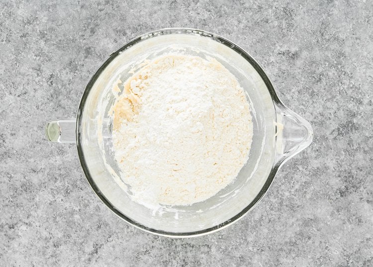 wet ingredients needed to make egg-free Hawaiian rolls in a stand mixer bowl with flour on top. 