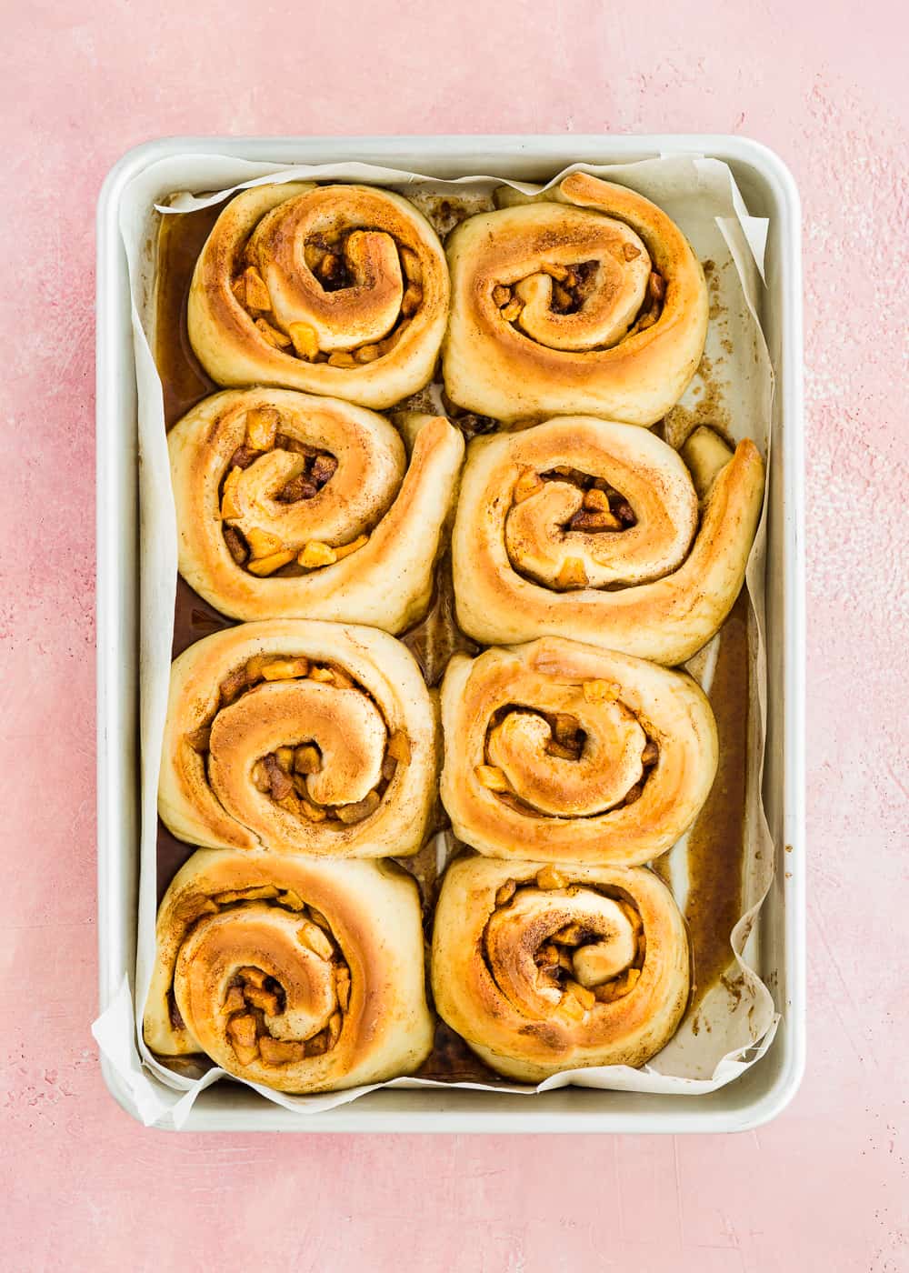 overhead view of baked eggless apple cinnamon rolls in a baking pan.