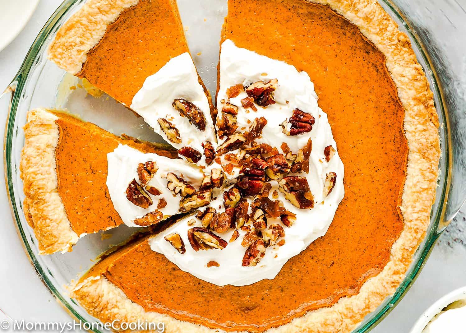 sliced egg free sweet potato pie with whipped cream and pecan on top in a pie dish. 