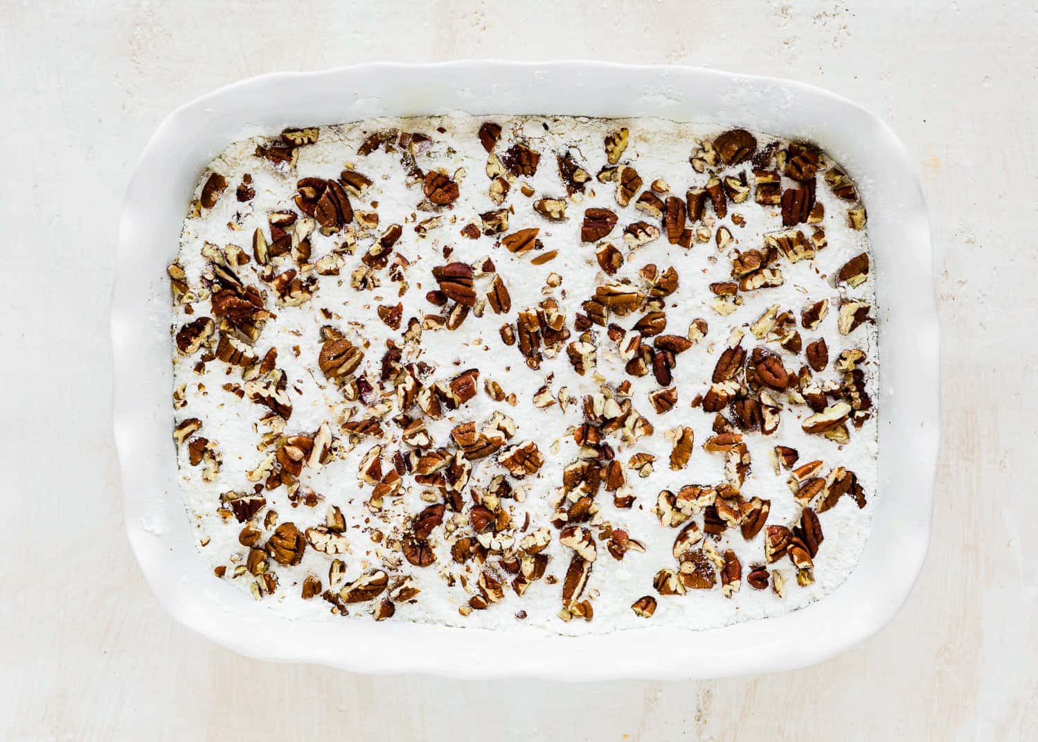 eggless dump cake mixture in a baking dish with a cake mix and pecans sprinkled on top.