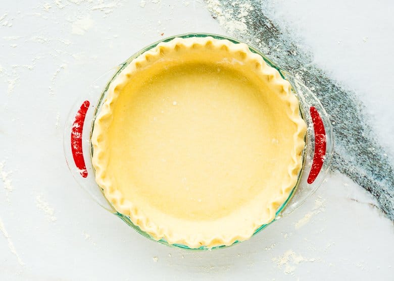 rolled out pie dough over a pie dish with crimping edges.