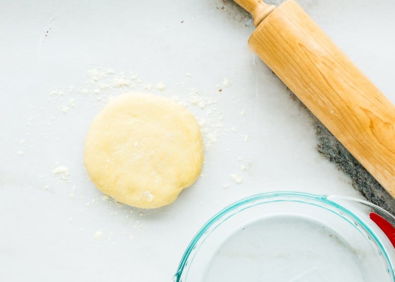 pie dough disk onto a floured surface with a rolling pin and a pie dish on the side. 