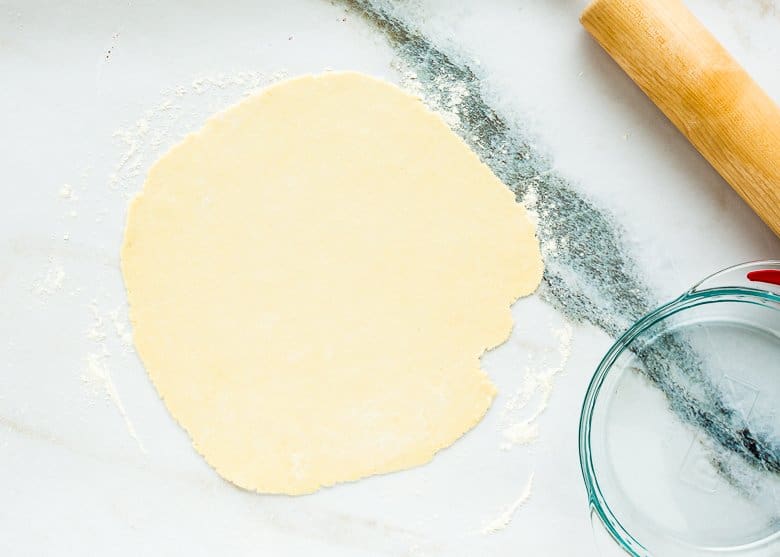 rolled out pie dough onto a floured surface with a rolling pin and a pie dish on the side. 