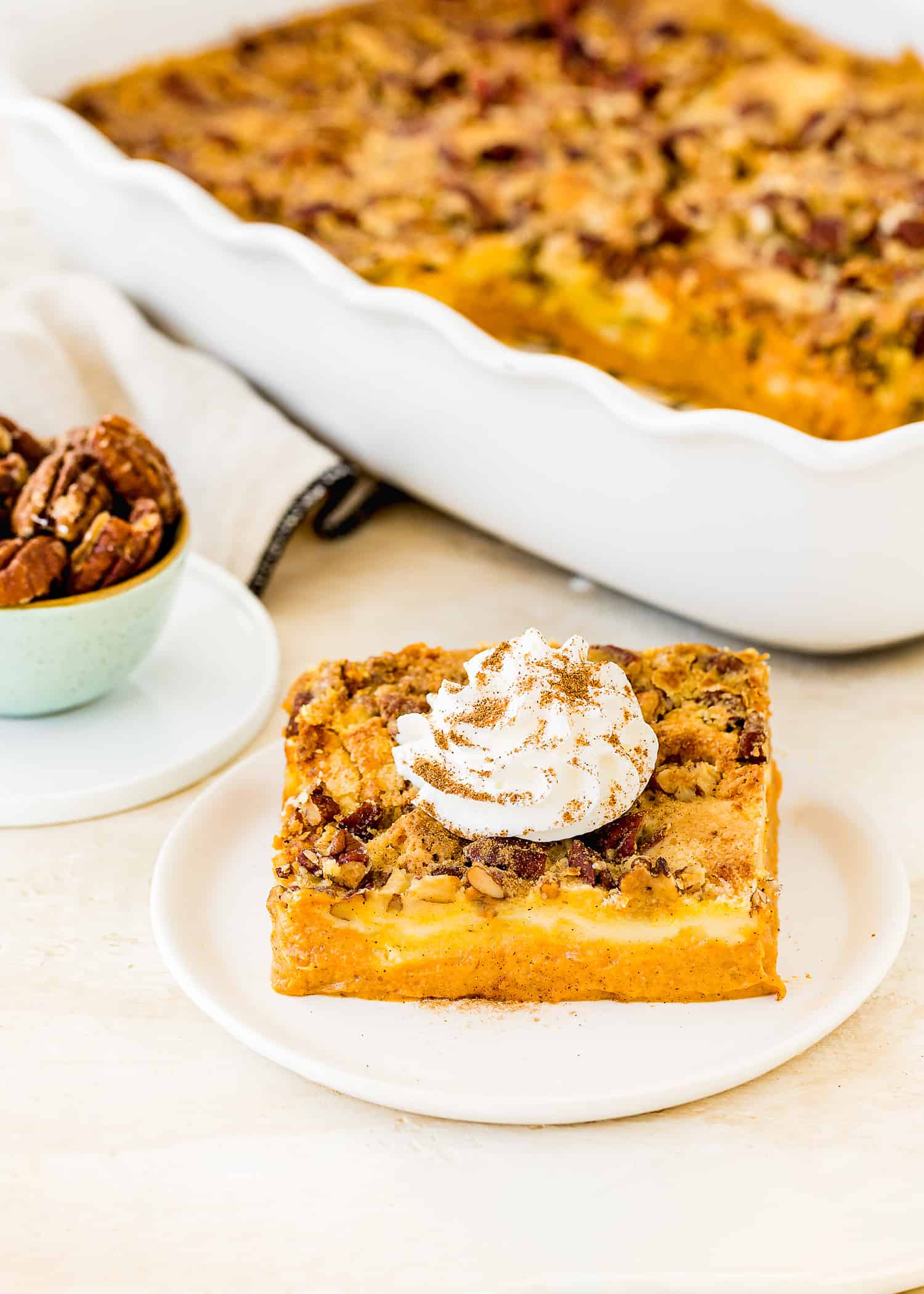 Eggless Pumpkin Dump Cake with whipped cream on a plate with the whole cake in a baking dish in the background.