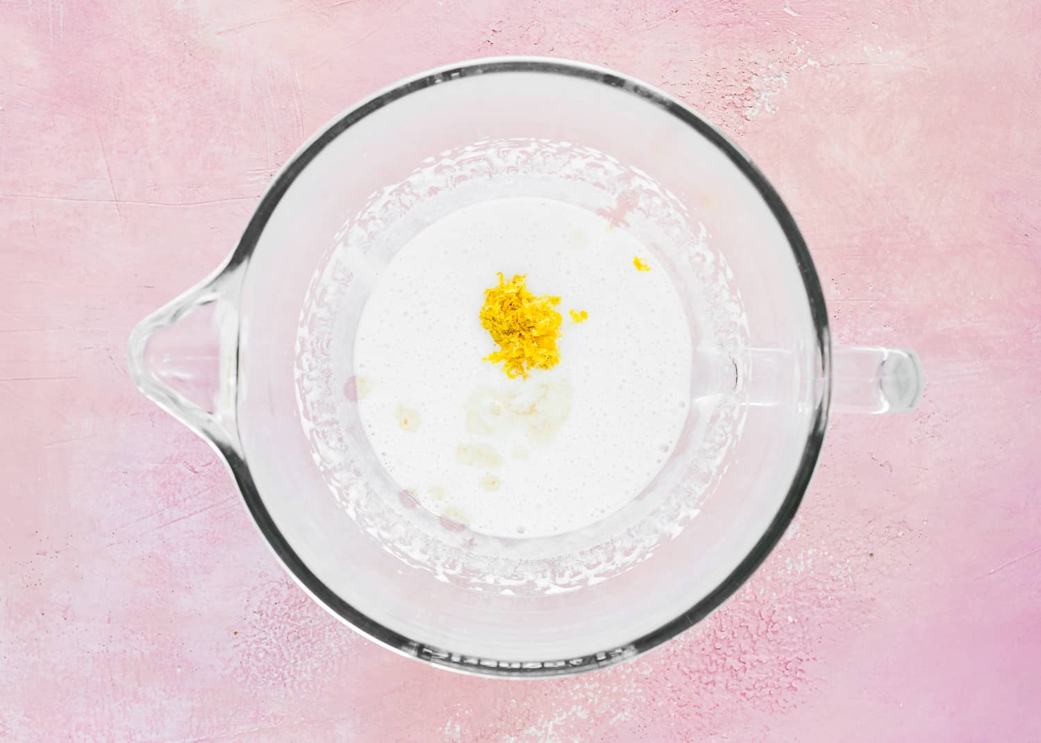 whipped aquafaba in a bowl of an stand mixer with lemon zest and vanilla extract on top. 