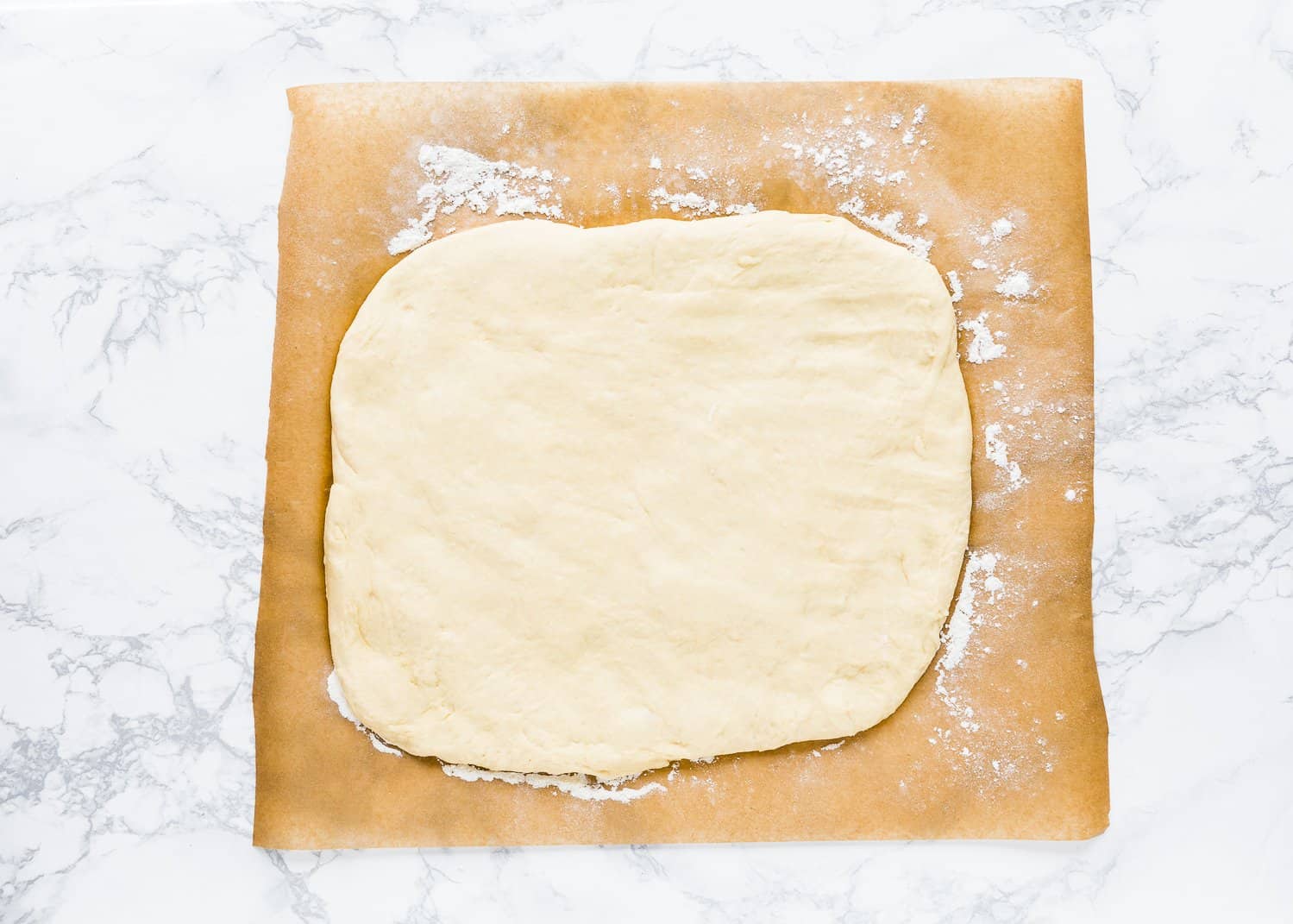 Egg-free monkey bread dough rolled out into a rectangle over a pieces of parchment paper. 