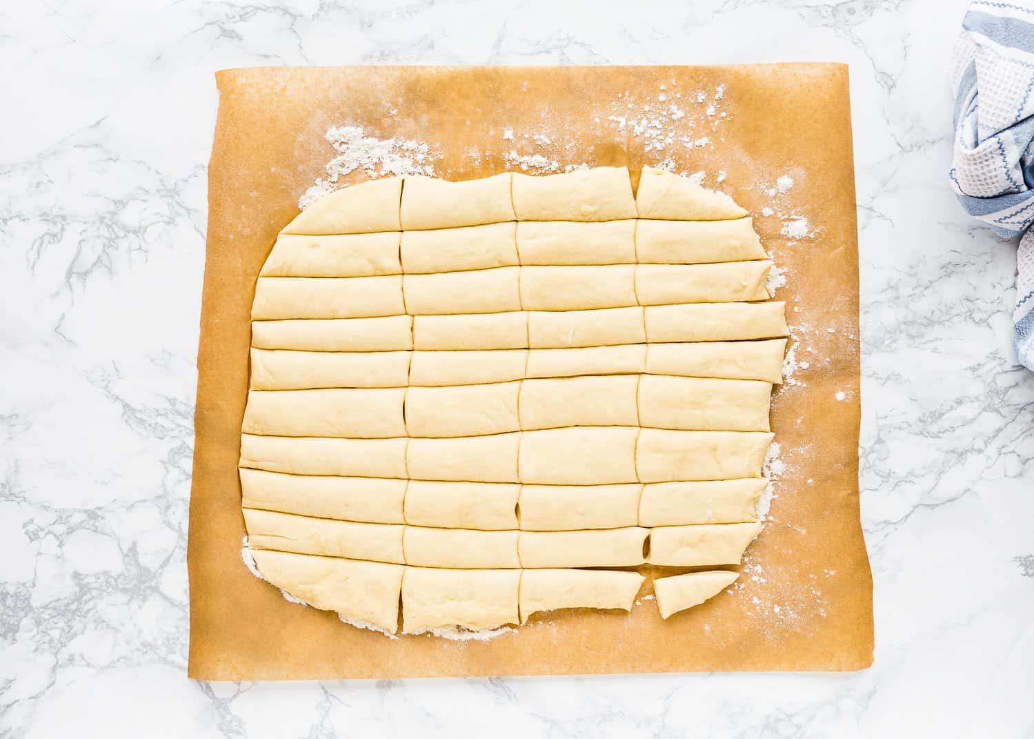 Egg-free monkey bread dough rolled out into a rectangle and cut into pieces over a pieces of parchment paper. 