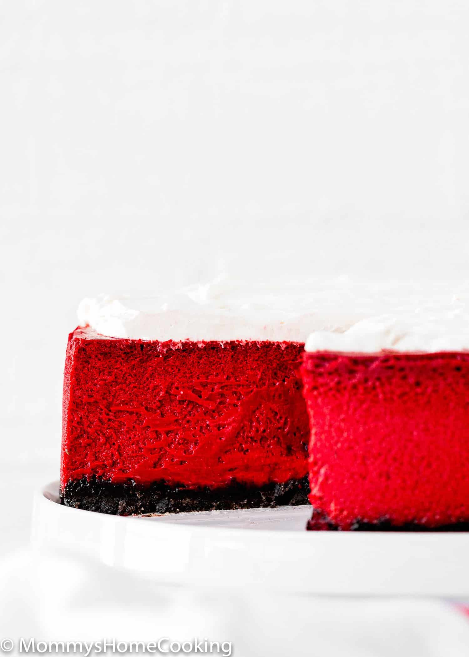 a sliced eggless Red Velvet Cheesecake topped with whipped cream on a plate. 