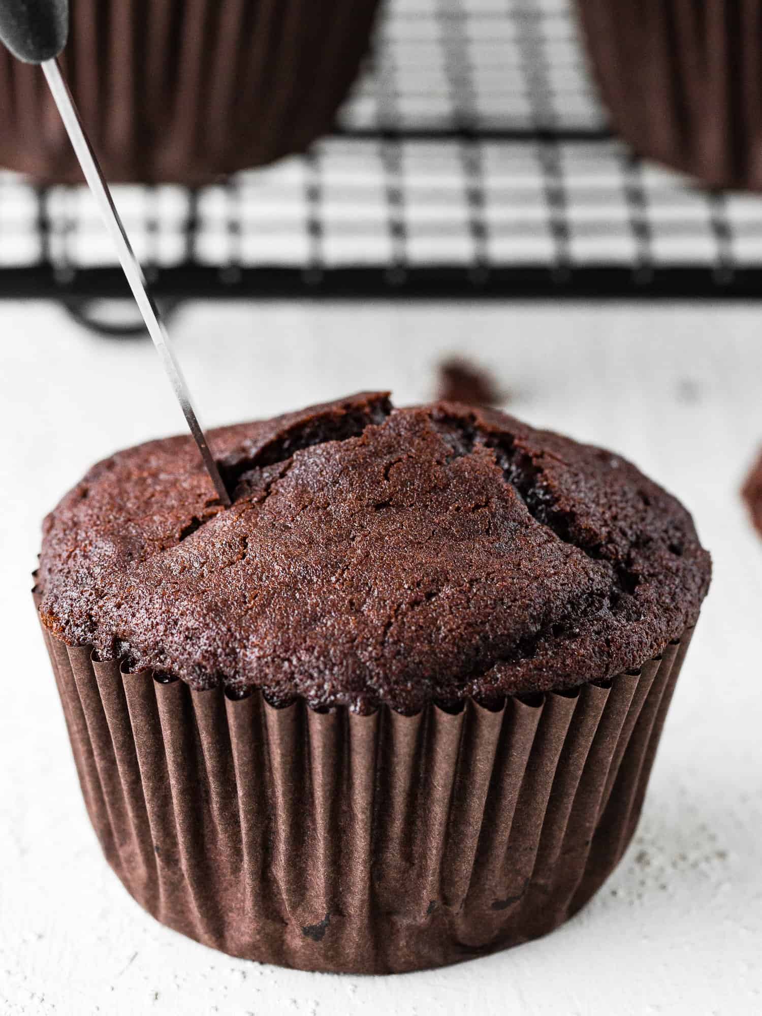 a knife cutting the top of an eggless chocolate cupcakes. 