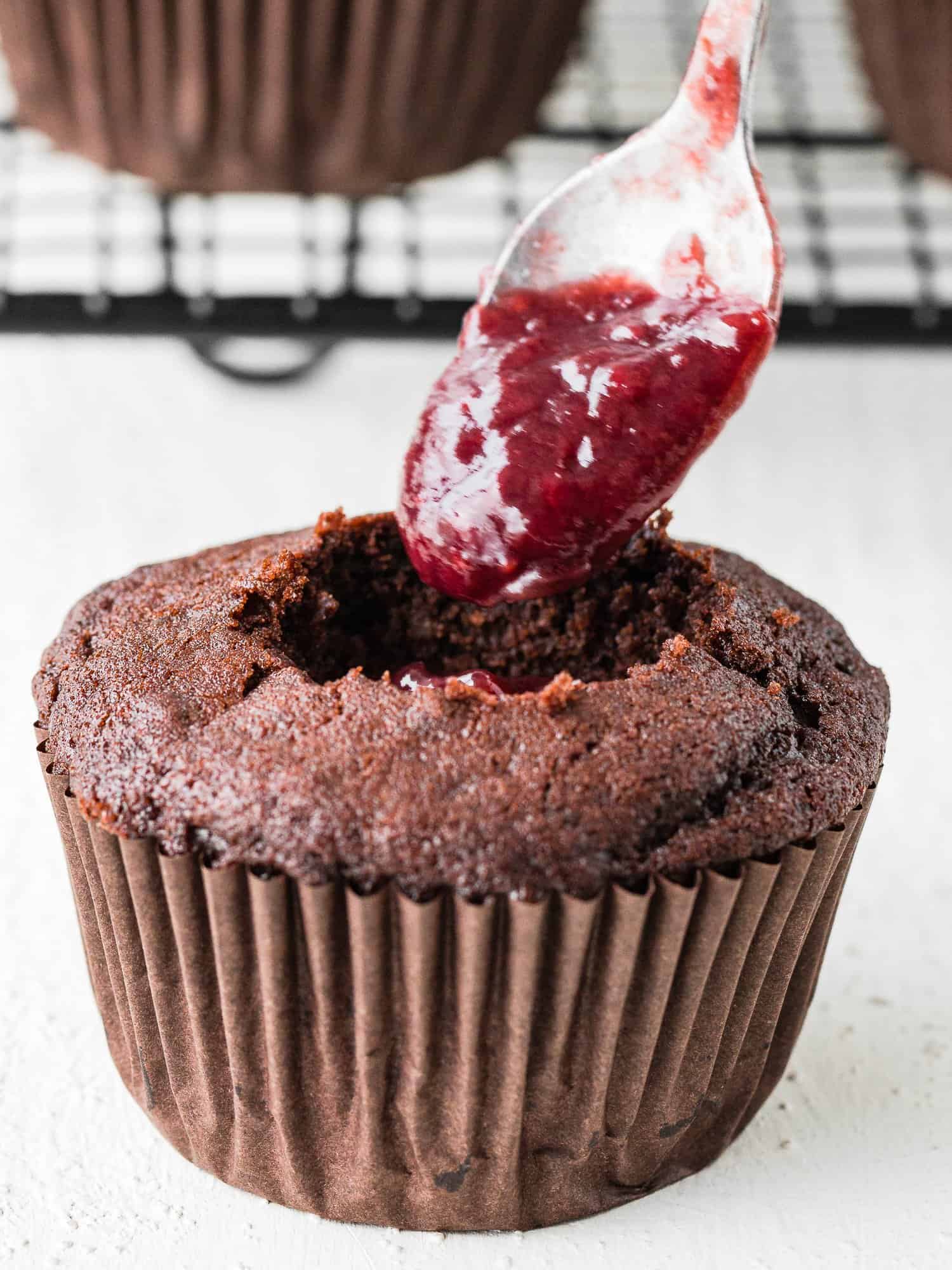 a spoon with Strawberry sauce filling an egg-free Chocolate cupcake center. 