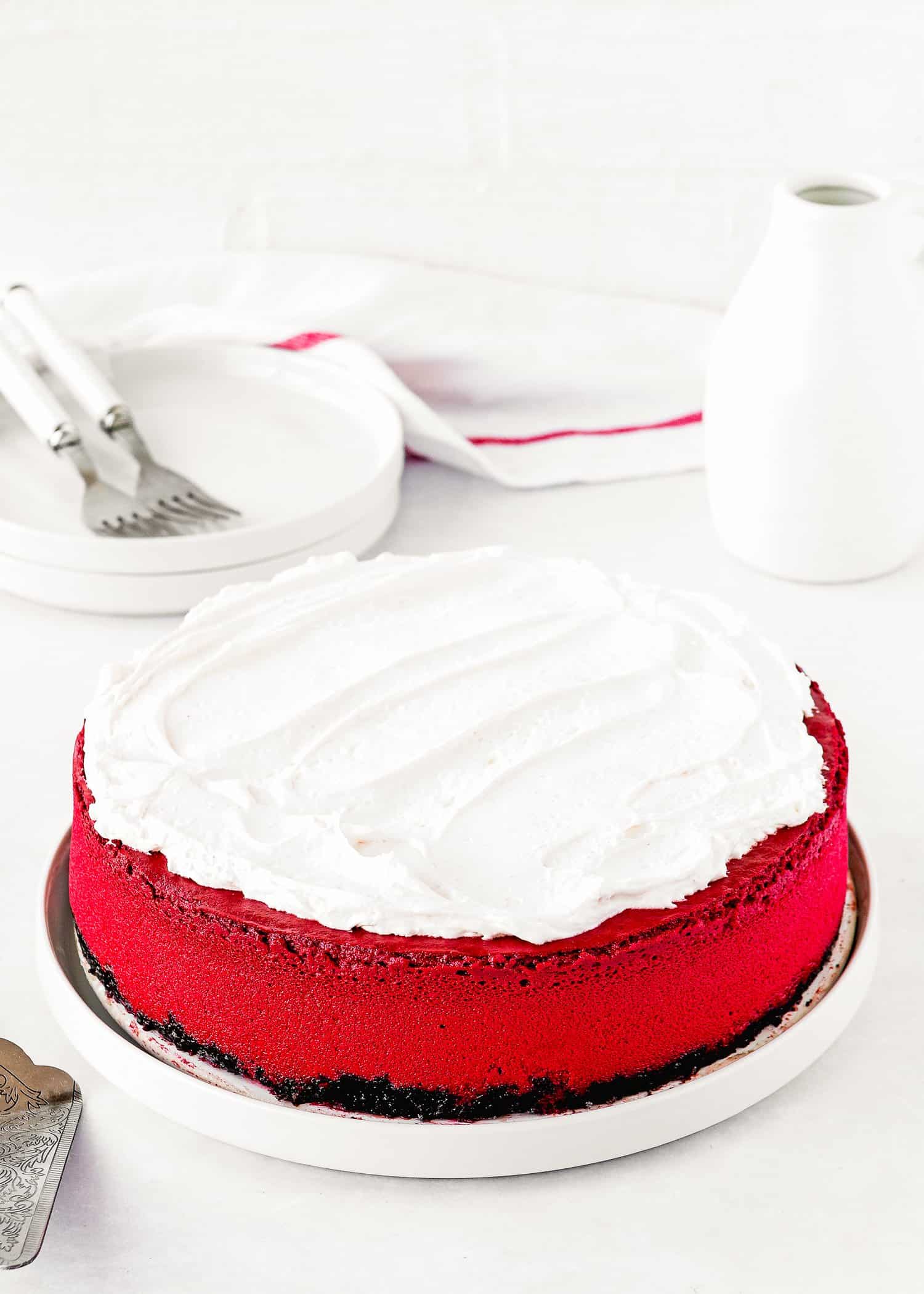 A whole Eggless Red Velvet Cheesecake topped with whipped cream on a plate. 