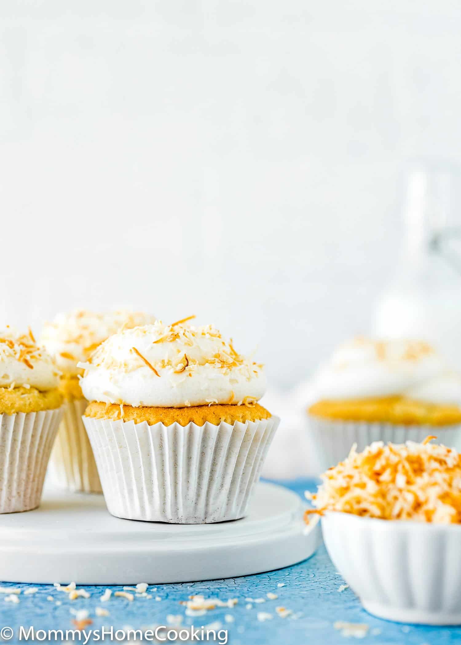 Eggless Coconut Cupcakes over a plate with buttercream and toasted coconut on top.