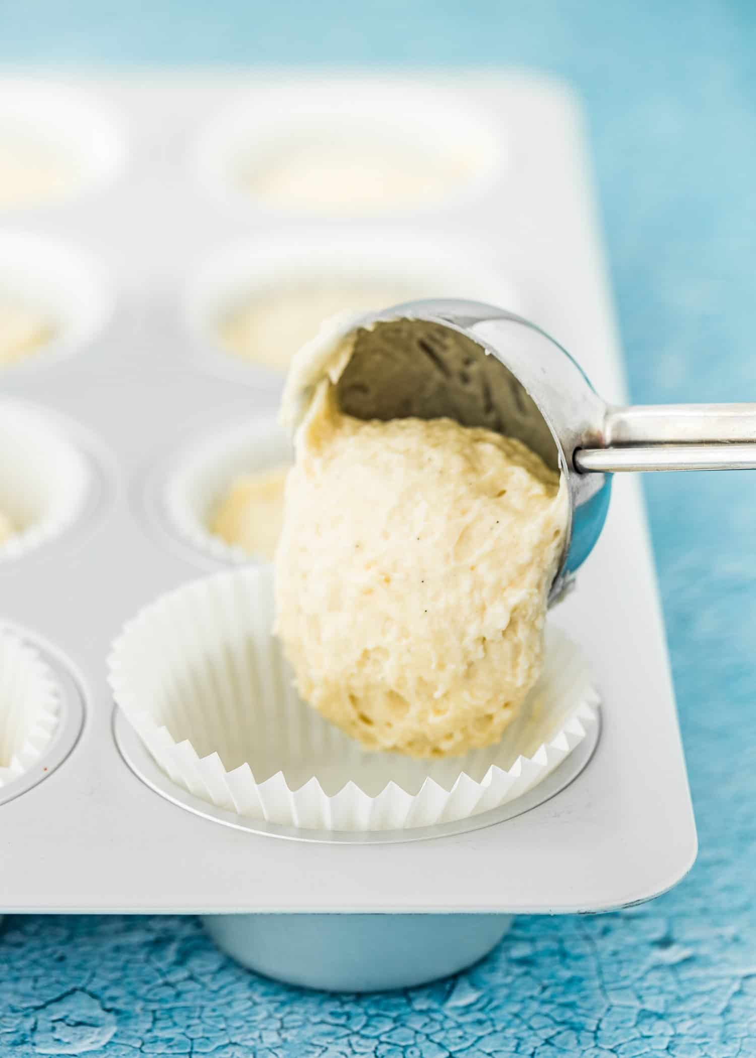 an ice cream scoop pouring egg-free cupcake batter into a cupcake pan.