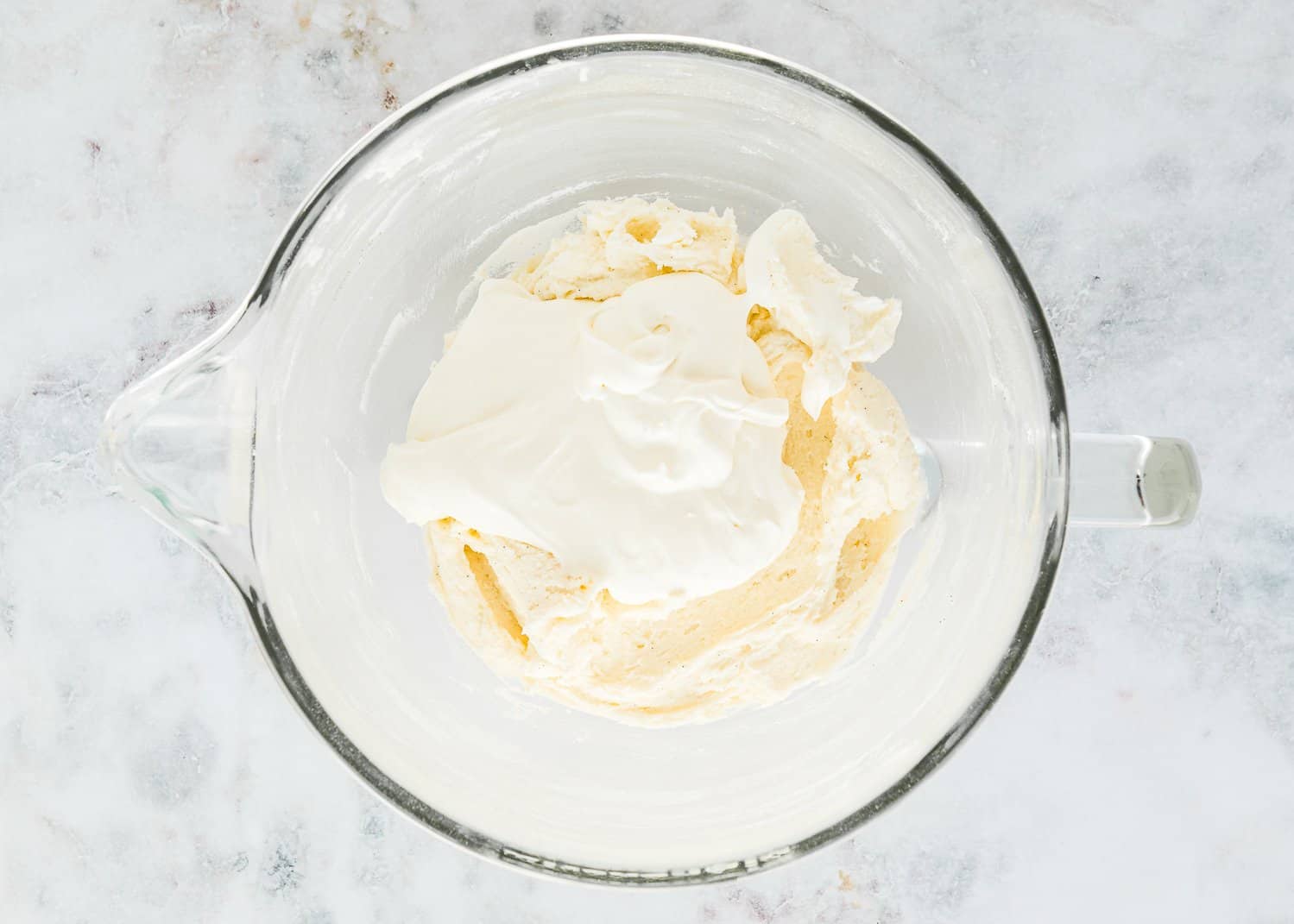 Whipped butter sugar, vanilla, and salt in a stand mixer bowl with cream cheese on top.