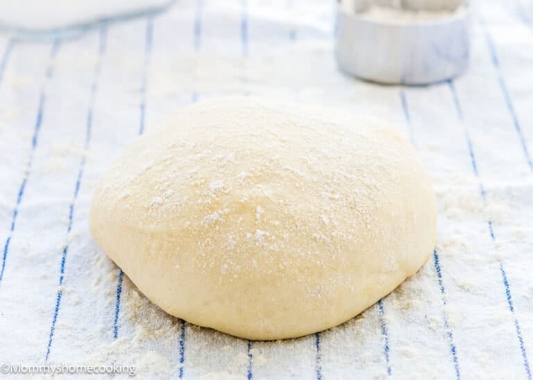 Ball of raw dough dusted with flour resting on a striped cloth, perfect for your favorite homemade pizza dough recipe, with a round metal cutter in the background.