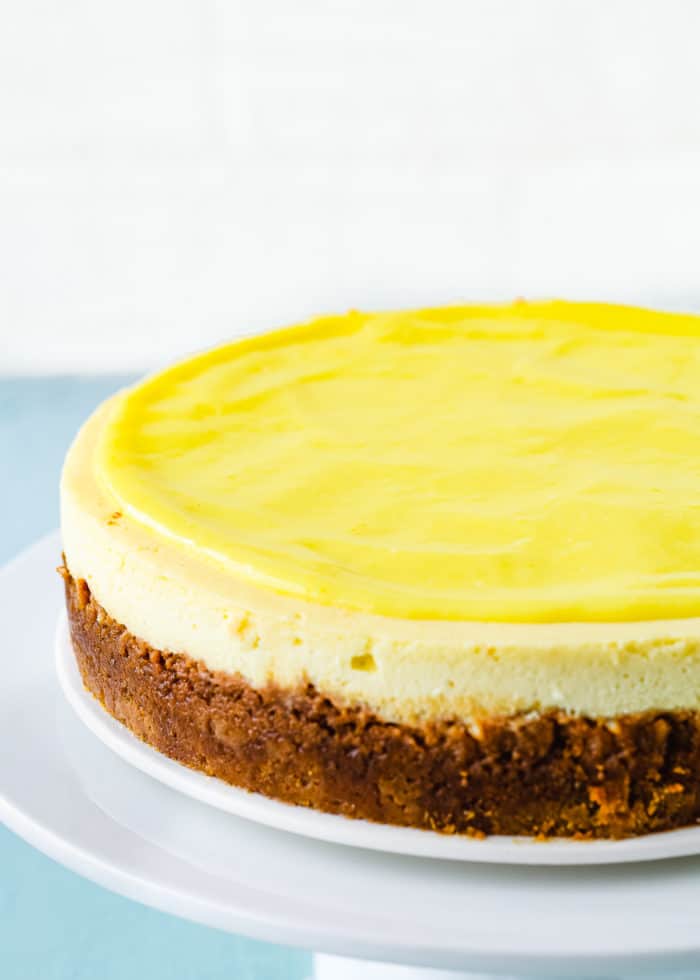 baked egg-free lemon cheesecake with egg-free lemon curd on top on a white plate. 