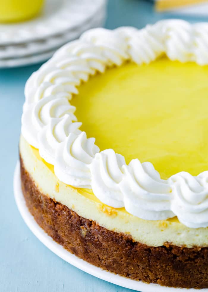 baked egg-free lemon cheesecake with egg-free lemon curd and whipped cream on top on a white plate. 