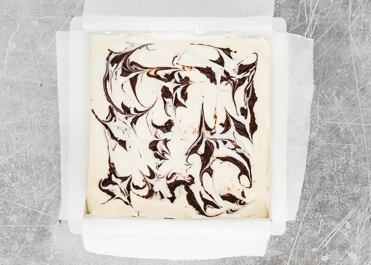 square baking pan with egg-free brownie batter, eggless Cheesecake batter and swirled dollops of egg-free brownie batter on top. 
