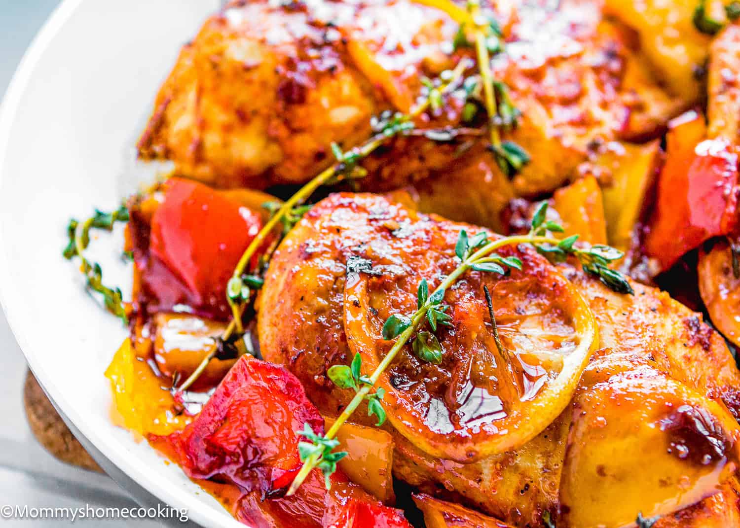 Close-up of The Juiciest Peri Peri Chicken Breasts (One Skillet), baked to perfection and garnished with lemon slices, fresh thyme, and surrounded by roasted red and yellow bell peppers.