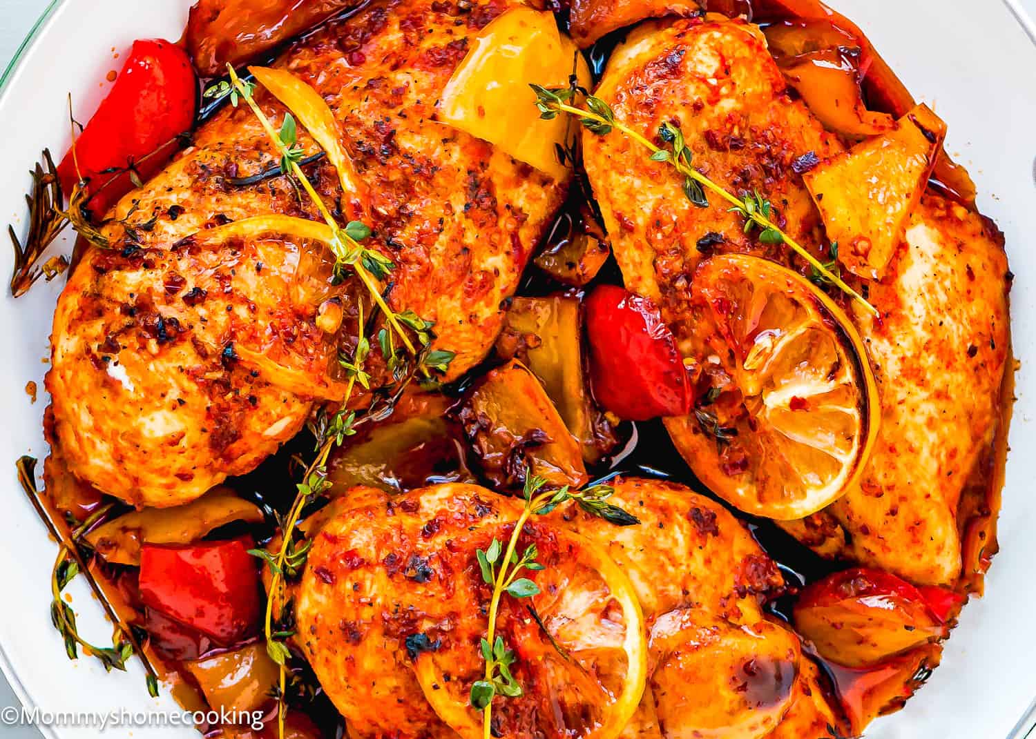 Baked Peri Peri Chicken Breasts with lemon slices, fresh thyme, and roasted red and yellow bell peppers on a white plate.