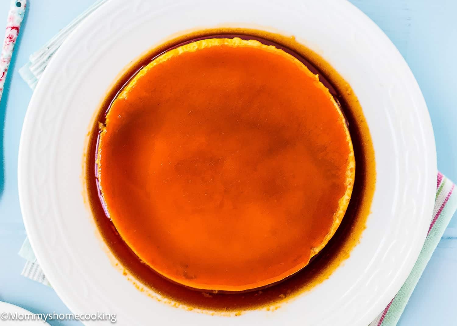 A round Venezuelan Flan Quesillo dessert with caramel sauce on top, served on a white plate.