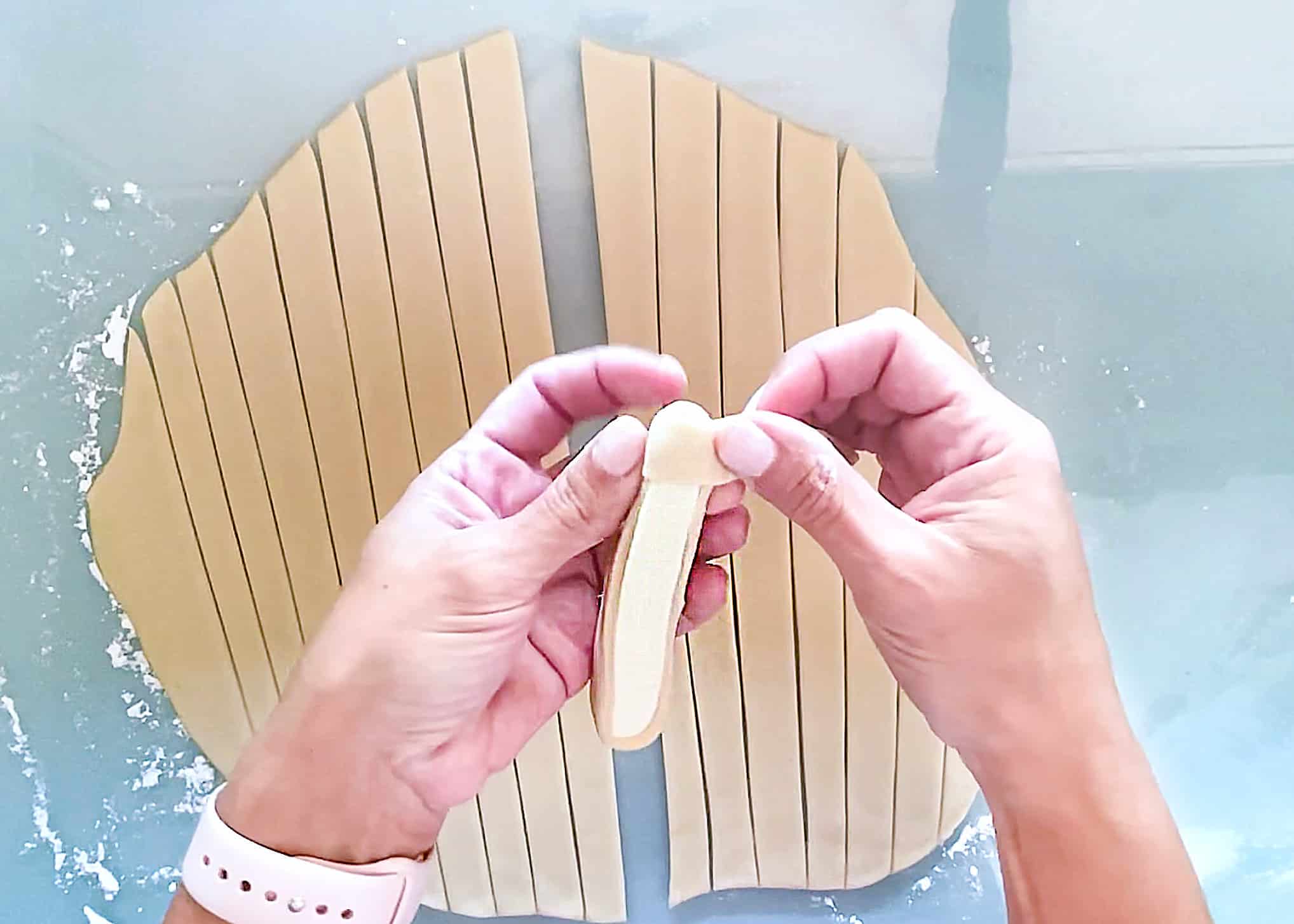 A hand holding a cheese stick and wrapping it with Venezuelan tequeño dough. 