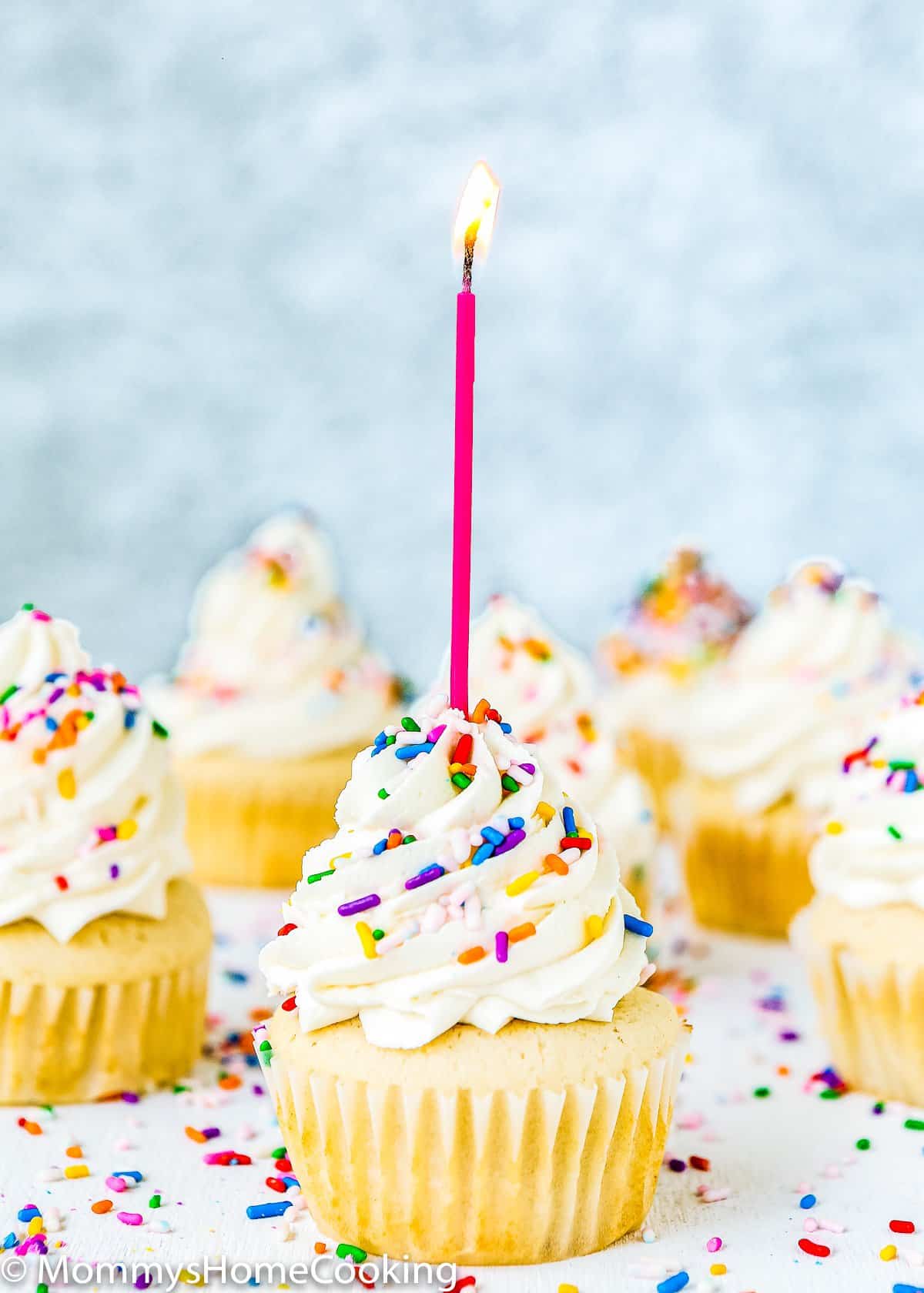 Vanilla cupcakes with frosting, sprinkles, and a candle.